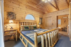 Un dormitorio de cabaña de madera con cama, mesita de noche, lámpara, espejo y ventana.