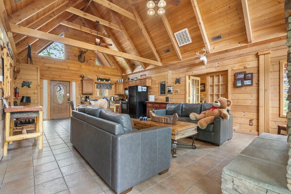 Ein Holzblockhaus-Interieur mit Essbereich, Küche und Wohnzimmer, möbliert mit Ledersofas und einer Bärenstatue.