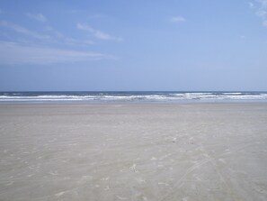 A wide sandy beach with gentle waves and a clear sky.