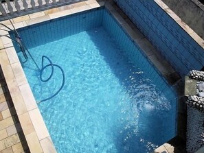 A rectangular swimming pool with clear blue water, tiled edges, and a visible hose on the left side.
