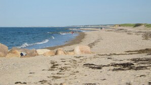 A sandy beach with rocks and waves, a clear sky, and distant buildings. - 18 Knott Ave (Sandwich)