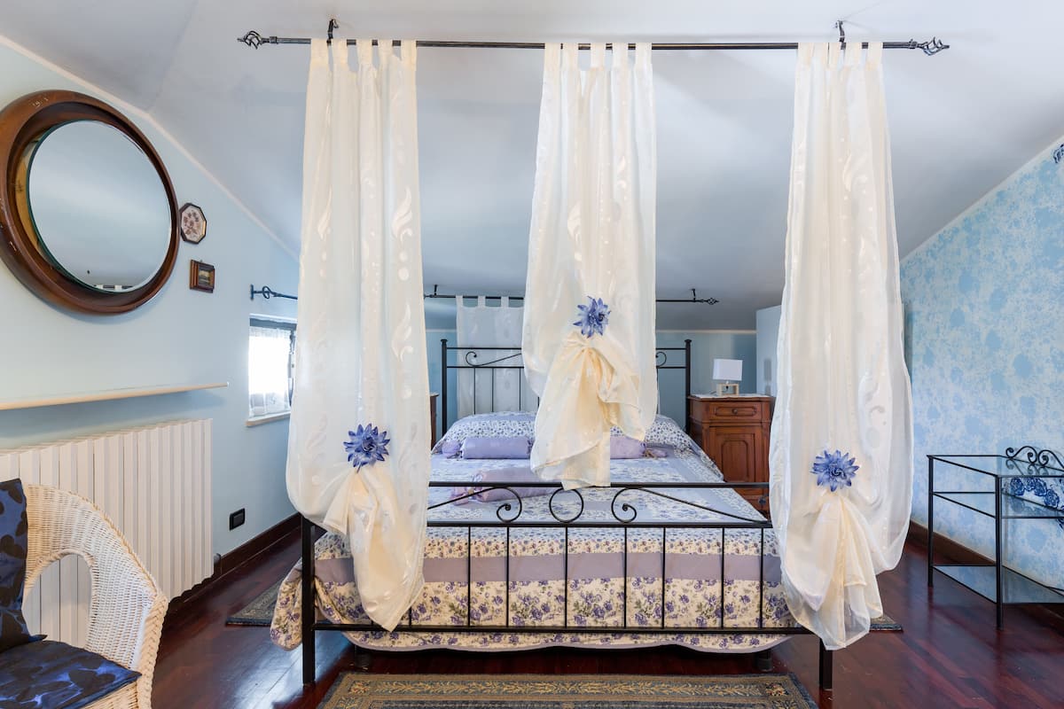 A four-poster canopy bed with floral decorations, a round mirror, and a wooden chair.