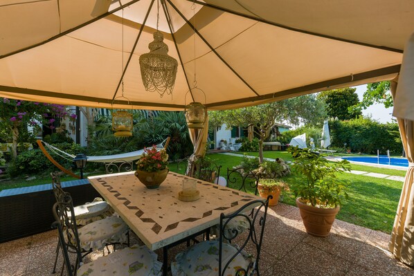 An outdoor patio with a table and chairs, surrounded by potted plants and a hanging light fixture. - Au Jardin Fleuri (San Giovanni Lupatoto)