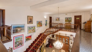 Interior de diversos nivells amb una escala de fusta, múltiples quadres emmarcats a les parets i un candelabrum.