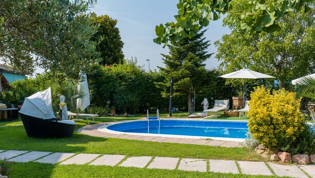 Una piscina envoltada per un jardí ben cuidat, un camí de pedra i mobiliari exterior.