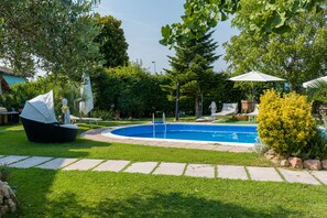 Piscina rodeada por césped cuidado, sendero de piedra y mobiliario exterior.