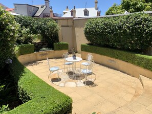 A patio with a round table and chairs, surrounded by neatly trimmed hedges and a tiled floor. - Kirribilli Luxury Grand Terrace House - your family oasis to explore Sydney (Sydney North)