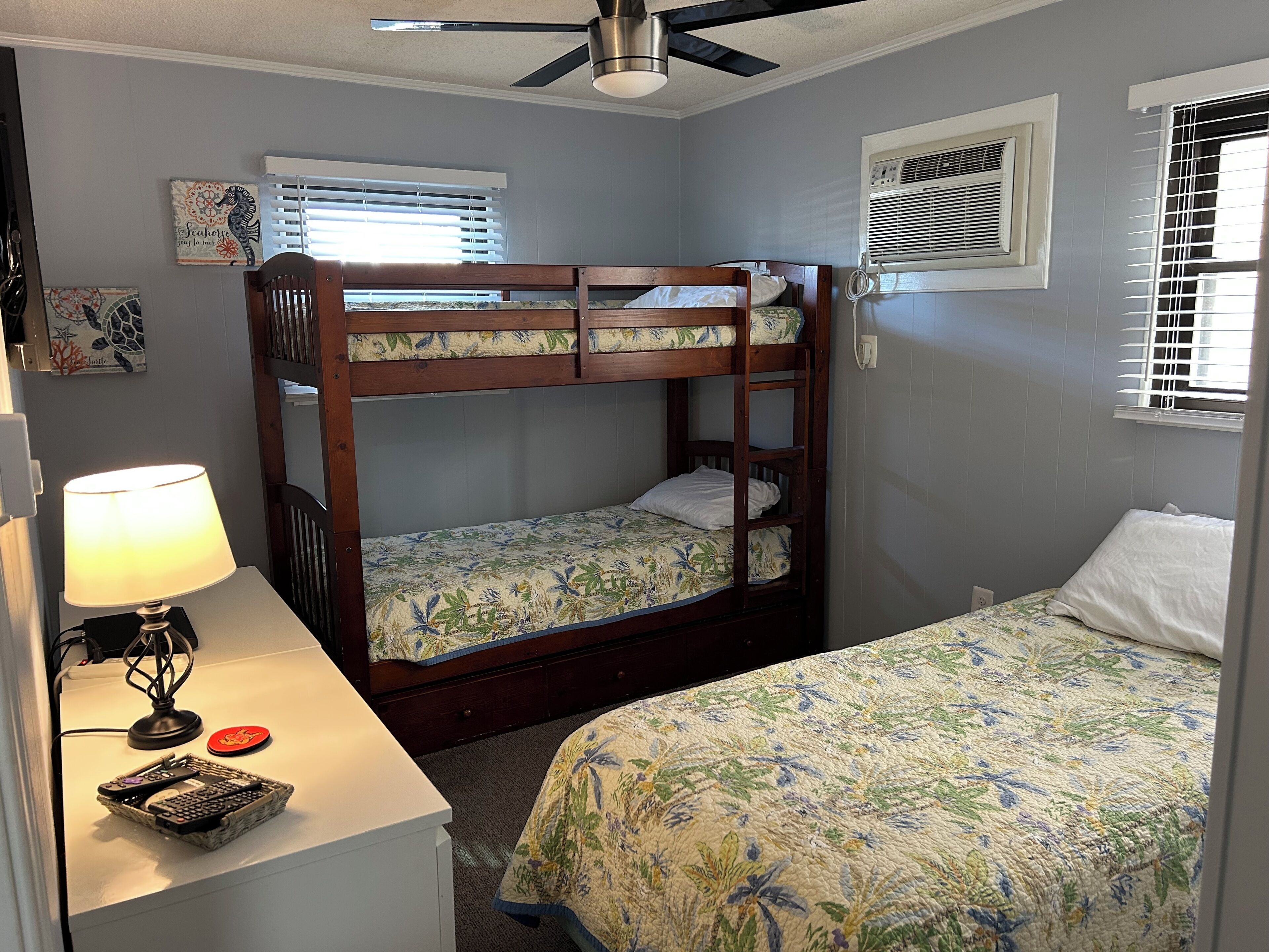 A bunk bed room with a desk, lamp, and artwork.