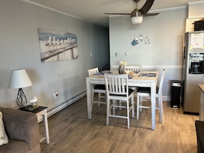 A dining area with a wooden table and chairs, a ceiling fan, a refrigerator, and a painting on the wall. - Luxurious Ocean View Condo - Cabana Beach  (Ocean City)