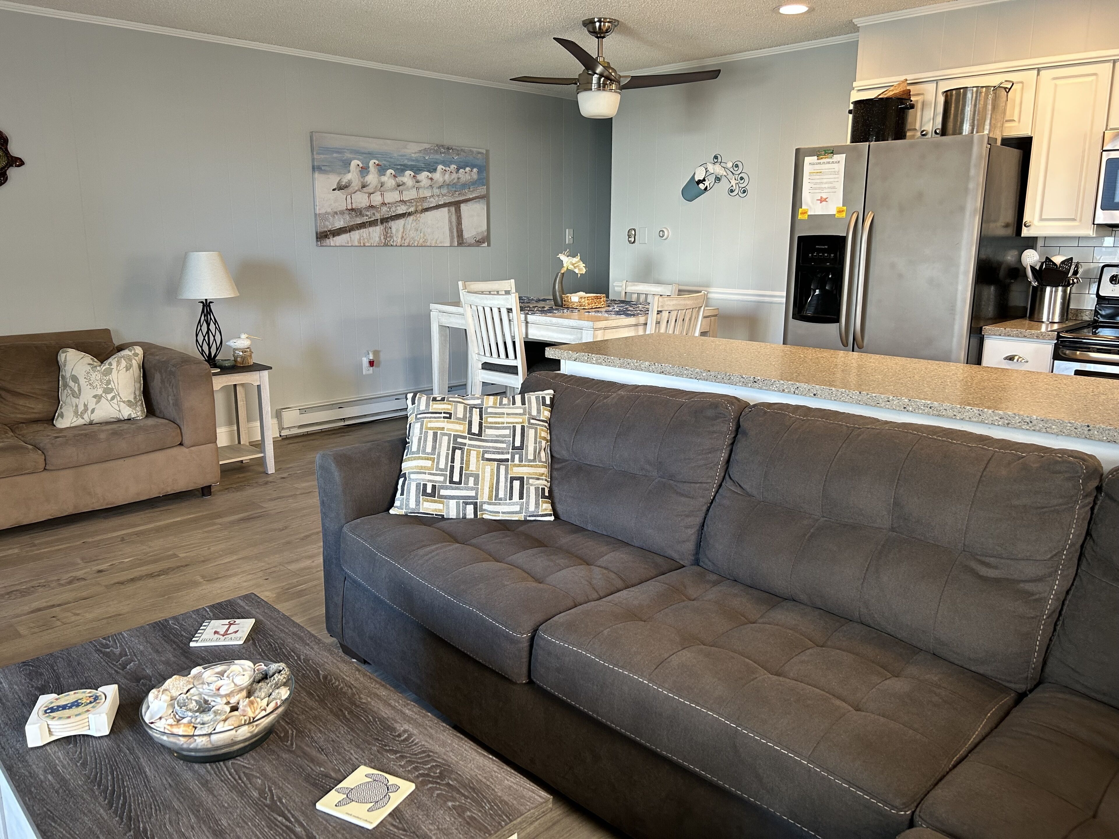 Een moderne woonkamer met een bruine bank, een salontafel met decoratieve objecten en een eethoek met een witte tafel en stoelen.