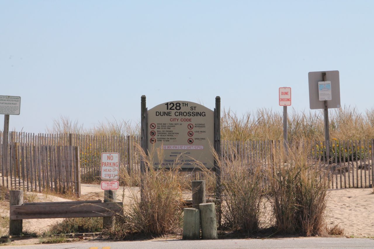 A beach entrance sign with beach rules and a wooden fence.