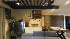 A modern living room with a pool table, a sofa, a large abstract painting, and a ceiling with a unique wooden design. - LAZY RIVER!  SLIDE and WATERFALLS!  GAMEROOM. (Palm Springs)
