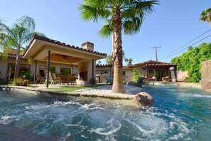 A pool with a waterfall feature, surrounded by a house with a covered patio and outdoor seating. - LAZY RIVER!  SLIDE and WATERFALLS!  GAMEROOM. (Palm Springs)