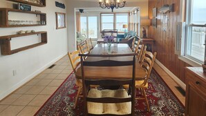 A dining room with a wooden table, chairs, a chandelier, and a view of the ocean through large windows. - Relax big in a small beach town! (Milford)