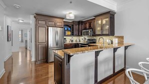 A modern kitchen with dark wood cabinets, stainless steel appliances, and a granite countertop island. - Luxury Waterfront Marina Condo in Downtown (Charlottetown)
