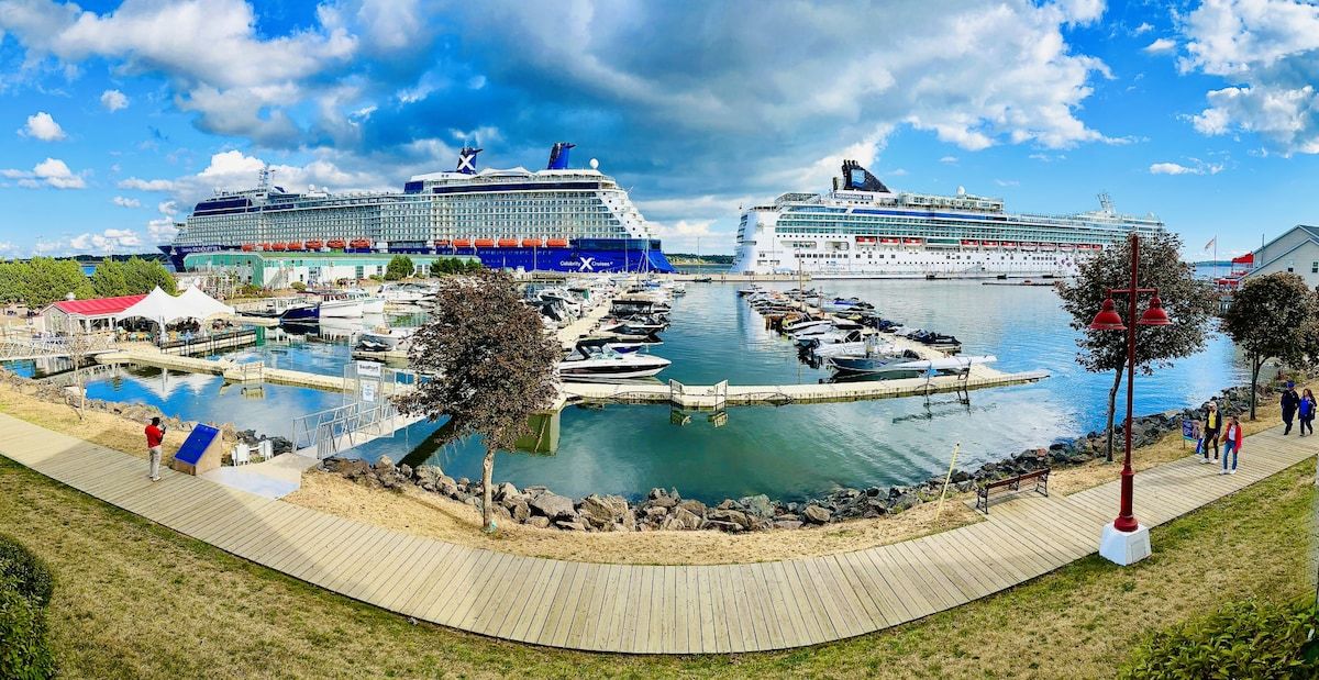 A marina with two large cruise ships docked, a wooden boardwalk, and a small building with a red roof.