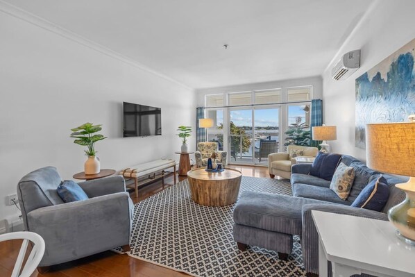 Uma sala de estar moderna com sofá, mesa de centro e vista para o exterior por grandes janelas.