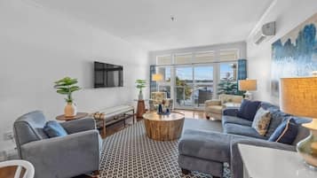 Ein modernes Wohnzimmer mit einer Couch, einem Sessel, einem Couchtisch und Blick ins Freie durch große Fenster.