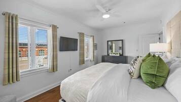 Ein Schlafzimmer mit Bett, Deckenventilator, Fernseher, Kommode und einem Fenster mit Vorhängen.