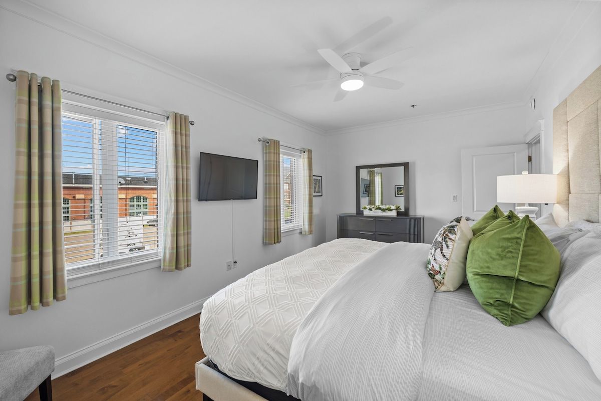 Quarto com cama, ventilador de teto, TV de tela plana e janela com cortinas.