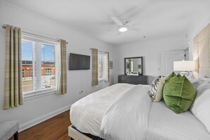 Quarto com cama, ventilador de teto, TV de tela plana e janela com cortinas.