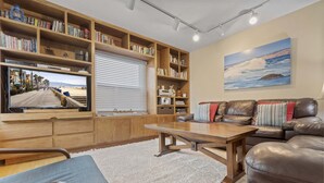 Ein Wohnzimmer mit Fernseher, Bücherregalen, einem Ledersofa und einem Bild an der Wand.