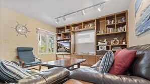 Ein Wohnzimmer mit einer Ledersofa, einem blauen Sessel, einem Holztisch, einem Bücherregal und einer Uhr an der Wand.