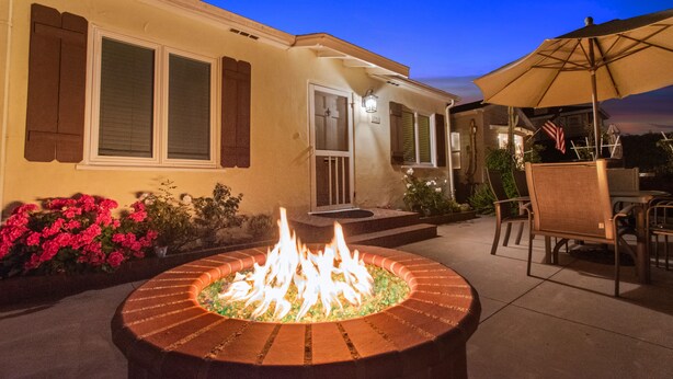 Eine Terrasse mit Feuerstelle, Gartenmöbeln und einem Haus mit beleuchtetem Eingang.