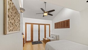 Ein Schlafzimmer mit einem Bett, einem Deckenventilator, einer Holztür und einer Wandleuchte.