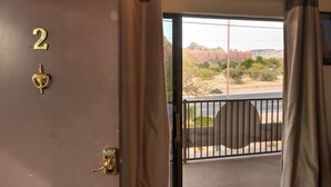 En hotelværelsesindgang med skilt med nummer 2, en dør med messinggreb og udsigt over et ørkenlandskab gennem en balkon med gelænder.