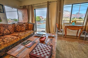 Una sala de estar con sofá, una mesa de centro con un tablero de ajedrez y vistas a un paisaje montañoso a través de ventanas amplias.