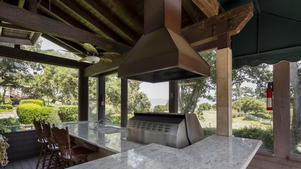 An outdoor kitchen area with a marble countertop, wooden chairs, and a view of the surrounding greenery. - Fantastic Vacation Retreat, Family Reunions , and Private Pool! (Salinas)
