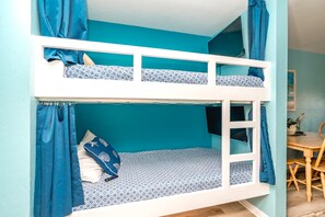 A bunk bed with a desk and chair, a television, and a plant in a room with teal walls. - The Lazy Palm - 1 BR Ocean View Surf Condo - Community Pool (Surf City)