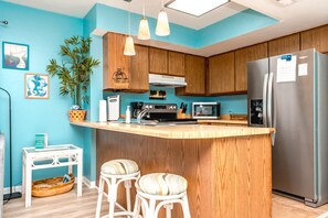 A kitchen with wooden cabinets, a stainless steel refrigerator, a microwave, and a bar stool.