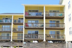 Edifício residencial de vários andares com varandas, cada uma com guarda-corpo de madeira e uma pequena mesa.