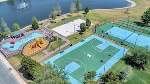 Vista aérea de un parque con cancha de baloncesto, parque infantil y un cuerpo de agua.