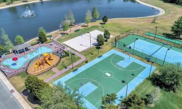 Vue aérienne d’un parc comprenant un terrain de basketball, une aire de jeux et un lac.