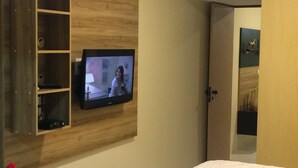 A hotel room with a mounted TV, a wooden shelf unit, a bed, and a door leading to another room. - Your rest in style! (GRAVATÁ)