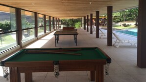 A pool area with a pool table and lounge chairs, large windows, and a view of a swimming pool and greenery. - Your rest in style! (GRAVATÁ)