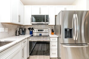 A modern kitchen with white cabinetry, a stainless steel refrigerator, a microwave, an oven, and a coffee maker.