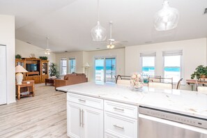 A spacious living area with a large kitchen island, wooden cabinets, and a view of the ocean through the sliding glass doors.