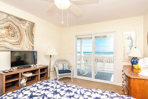 A hotel room with a large bed, a television, a chair, a desk, and a balcony with a view of the ocean. - Happy Days - Endless Ocean Views; 3BR; Easy Beach Access (North Topsail Beach)