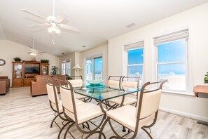 A spacious living area with a glass-top dining table surrounded by chairs, a ceiling fan, and a television on a wooden cabinet. - Happy Days - Endless Ocean Views; 3BR; Easy Beach Access (North Topsail Beach)
