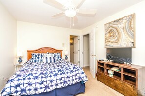 A bedroom with a bed, a ceiling fan, a TV stand, and a door.