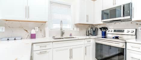 A modern kitchen with white cabinets, a stainless steel range, and a microwave.