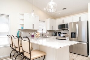 Una cocina moderna con armarios blancos, un refrigerador de acero inoxidable, un microondas integrado y una cafetera.