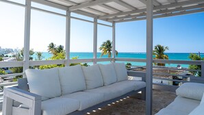 A covered outdoor seating area with a white sofa and a view of the ocean. - Welcome to the Lucky Penny! (Ocean Park)