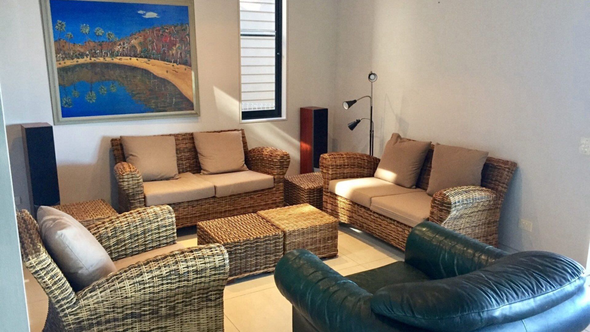 A living room with wicker furniture, a painting on the wall, and a floor lamp.
