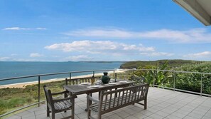 Un balcon avec une table et des chaises donnant sur une plage et l’océan.