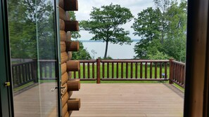 Eine Holzdielen-Terrasse mit Geländer, mit Blick auf einen See und Bäume.